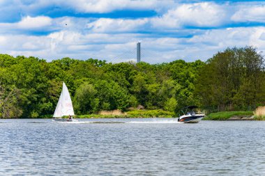 Bulutlu bir günde, yeşil ağaçların ve çalıların önünde akmakta olan iki yüzen kayıkla dolu güzel bir manzara.
