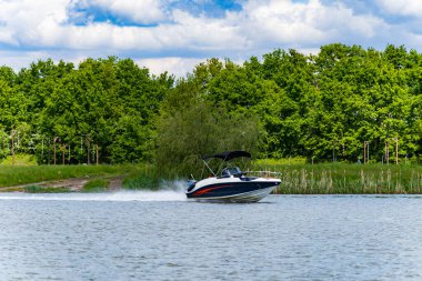 Geniş nehirde çok hızlı yüzen küçük bir tekne. Arkasında yeşil ağaçlar ve çalılar var. Bulutlu bir sabahta kontrolü elinde tutan bir adam var.
