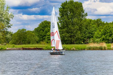 Wroclaw, Polonya - 14 Mayıs 2023: Bulutlu bir günde Odra nehrinde yeşil ağaçlar ve çalılarla yüzen Sagitta adlı küçük beyaz tekne