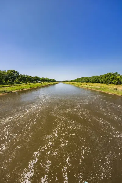 stock image Beautiful landscape of long dirty river with green trees and bushes on both sides seen from bridge over water dam and water level