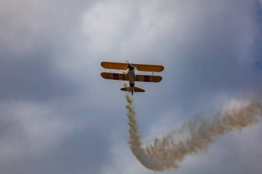 Leszno, Polonya - 16 Haziran 2023: Antidotum Airshow Leszno 2023 ve mavi bulutlu gökyüzünde sarı Boeing Stearman uçağı akrobatik gösterileri