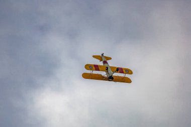 Leszno, Polonya - 16 Haziran 2023: Antidotum Airshow Leszno 2023 ve mavi bulutlu gökyüzünde sarı Boeing Stearman uçağı akrobatik gösterileri