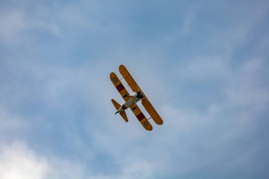 Leszno, Polonya - 16 Haziran 2023: Antidotum Airshow Leszno 2023 ve mavi bulutlu gökyüzünde sarı Boeing Stearman uçağı akrobatik gösterileri