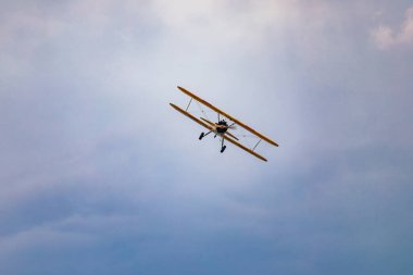Leszno, Polonya - 16 Haziran 2023: Antidotum Airshow Leszno 2023 ve mavi bulutlu gökyüzünde sarı Boeing Stearman uçağı akrobatik gösterileri