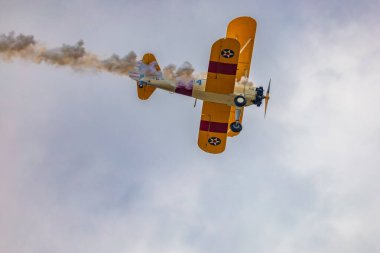 Leszno, Polonya - 17 Haziran 2023: Antidotum Airshow Leszno 2023 ve mavi bulutlu gökyüzünde sarı Boeing Stearman uçağı akrobatik gösterileri