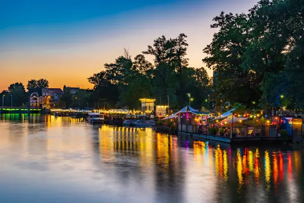Wroclaw, Polonya - 25 Haziran 2023: Adanın yanındaki sudaki modern bar ve restoranların cepheleri ve etrafındaki küçük parlak ışıklarla dolu