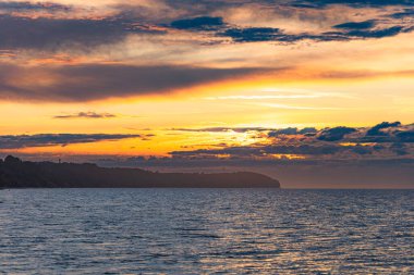 Yazın fırtınadan ve yağmurdan hemen sonra, kumsalda, karanlık ve soğuk denizin yanında, altın rengi güzel bir gün batımı.