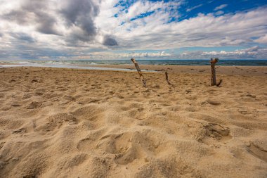 Fırtınalı denizin güzel manzarası kum tepecikleriyle dolu büyük kumsaldan görünüyor ve yere üç büyük kazık çakılıyor.