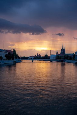 Wroclaw, Polonya - 13 Temmuz 2023: Odra nehri üzerinde güzel ve renkli gün batımı batıdan yaklaşan yağış Grunwaldzki köprüsünden görülüyor