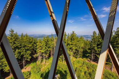 Walbrzych, Poland - August 14 2023: Beautiful green and blue landscape full of high trees and mountains seen from behind bars of viewing tower on top of Borowa mountain