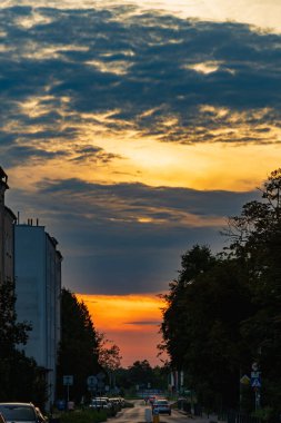 Wroclaw, Poland - August 24 2023: Beautiful cloudy sunset at afternoon with dark cloudy sky over long street high green trees and bushes