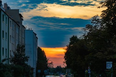 Wroclaw, Poland - August 24 2023: Beautiful cloudy sunset at afternoon with dark cloudy sky over long street high green trees and bushes