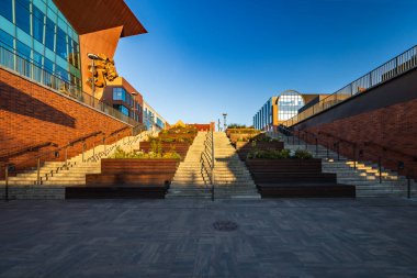 Gdansk, Polonya - 6 Eylül 2023: Merdivenlerde ahşap banklar ve güneşli bir sabahta Sienna Targ Meydanı 'nda çiçekler bulunan güzel bir meydan