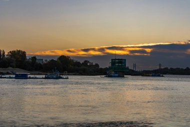 Varşova, Polonya - 15 Ekim 2023: Altın bulutlu güzel bulutlu gün doğumu ve Pinsk Flotilla Bulvarı 'ndan soğuk bir sabah görülen uzun Vistula nehri üzerinde yükselen güneş