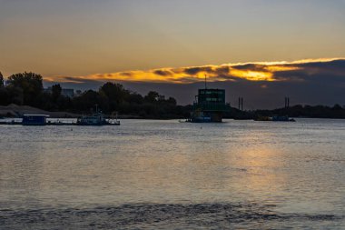 Varşova, Polonya - 15 Ekim 2023: Altın bulutlu güzel bulutlu gün doğumu ve Pinsk Flotilla Bulvarı 'ndan soğuk bir sabah görülen uzun Vistula nehri üzerinde yükselen güneş