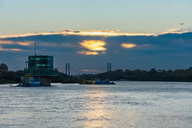 Varşova, Polonya - 15 Ekim 2023: Altın bulutlu güzel bulutlu gün doğumu ve Pinsk Flotilla Bulvarı 'ndan soğuk bir sabah görülen uzun Vistula nehri üzerinde yükselen güneş