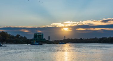 Varşova, Polonya - 15 Ekim 2023: Altın bulutlu güzel bulutlu gün doğumu ve Pinsk Flotilla Bulvarı 'ndan soğuk bir sabah görülen uzun Vistula nehri üzerinde yükselen güneş