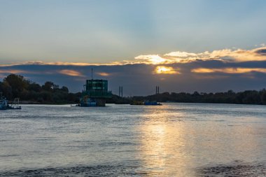 Varşova, Polonya - 15 Ekim 2023: Altın bulutlu güzel bulutlu gün doğumu ve Pinsk Flotilla Bulvarı 'ndan soğuk bir sabah görülen uzun Vistula nehri üzerinde yükselen güneş