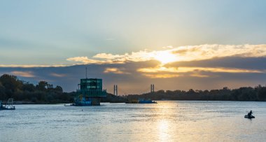 Varşova, Polonya - 15 Ekim 2023: Altın bulutlu güzel bulutlu gün doğumu ve Pinsk Flotilla Bulvarı 'ndan soğuk bir sabah görülen uzun Vistula nehri üzerinde yükselen güneş