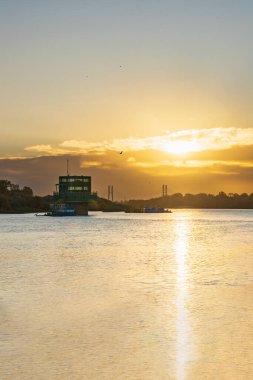 Varşova, Polonya - 15 Ekim 2023: Altın bulutlu güzel bulutlu gün doğumu ve Pinsk Flotilla Bulvarı 'ndan soğuk bir sabah görülen uzun Vistula nehri üzerinde yükselen güneş