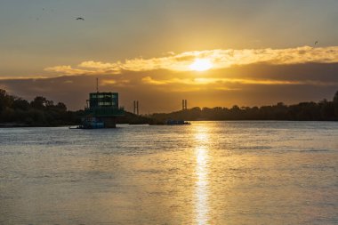 Varşova, Polonya - 15 Ekim 2023: Altın bulutlu güzel bulutlu gün doğumu ve Pinsk Flotilla Bulvarı 'ndan soğuk bir sabah görülen uzun Vistula nehri üzerinde yükselen güneş