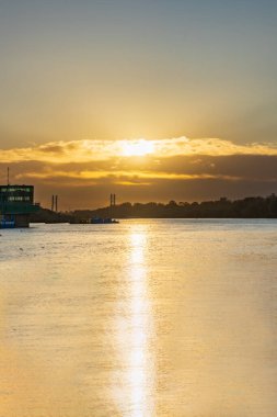 Varşova, Polonya - 15 Ekim 2023: Altın bulutlu güzel bulutlu gün doğumu ve Pinsk Flotilla Bulvarı 'ndan soğuk bir sabah görülen uzun Vistula nehri üzerinde yükselen güneş