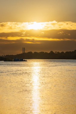 Varşova, Polonya - 15 Ekim 2023: Altın bulutlu güzel bulutlu gün doğumu ve Pinsk Flotilla Bulvarı 'ndan soğuk bir sabah görülen uzun Vistula nehri üzerinde yükselen güneş