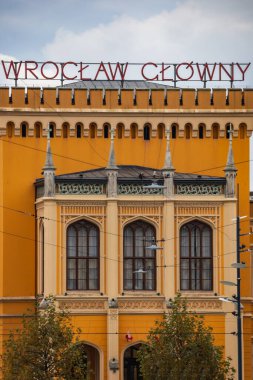 Wroclaw, Polonya - 12 Kasım 2023: Sokağın sonundaki ana tren istasyonu binasının güzellikle yenilenmiş ön cephesi ve gece vakti üzerinde logo bulunan büyük bir parıltı 