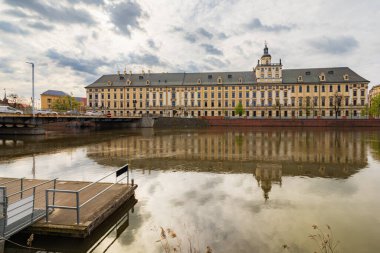 Wroclaw, Polonya - 6 Nisan 2024: Wroclaw 'daki görkemli üniversite Odra Nehri' nin sakin sularına yansıyarak çarpıcı bir şehir manzarası yaratıyor.