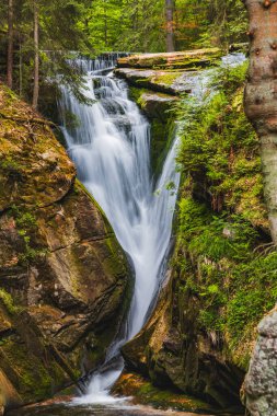 Beautiful giant Szklarka waterfall with giant rocks around and green surroundings clipart