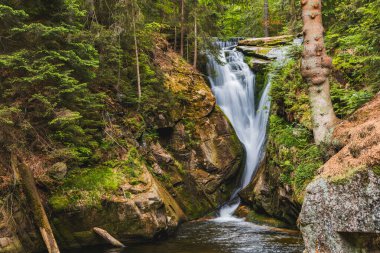 Beautiful giant Szklarka waterfall with giant rocks around and green surroundings clipart