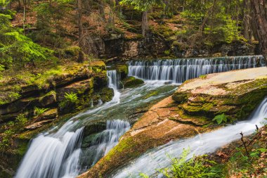 Beautiful giant Szklarka waterfall with giant rocks around and green surroundings clipart