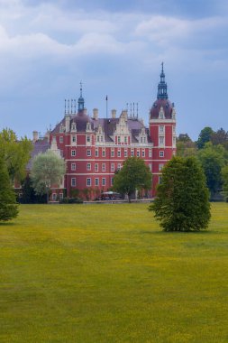 Bad Muskau, Germany - May 3 2024: Beautiful and majestic Hermann von Puckler's Castle at center of Muskau park with beautiful green glades around and reflecting in small pond clipart