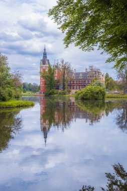 Bad Muskau, Germany - May 3 2024: Beautiful and majestic Hermann von Puckler's Castle at center of Muskau park with beautiful green glades around and reflecting in small pond clipart