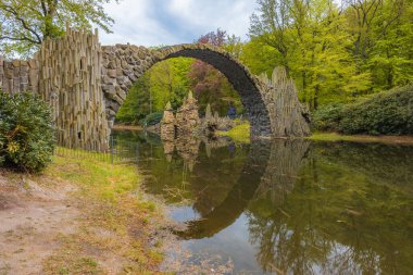 Kromlau, Almanya - 3 Mayıs 2024: Rododendron ve Azalea Bahçesi, kemerli köprüler, göletler, tarihi bir konut ve sayısız rhododendron ile iyi korunan 19. yüzyıl parkı