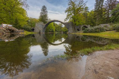 Kromlau, Almanya - 3 Mayıs 2024: Rododendron ve Azalea Bahçesi, kemerli köprüler, göletler, tarihi bir konut ve sayısız rhododendron ile iyi korunan 19. yüzyıl parkı