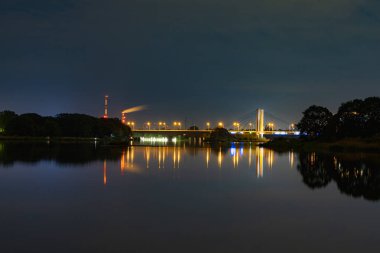 Wroclaw, Polonya - 11 Mayıs 2024: Bulutlu ve yıldızlı bir gecede, sessiz Odra nehrine yansıyan Milenyum köprüsü ile yüksek ağaç ve çalıların güzel gece manzarası