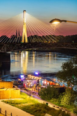 Warsaw, Poland - June 12 2024: Illuminated Swietokrzyski Bridge and Riverside Restaurant at Warsaw Sunset clipart