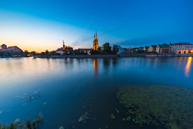 Wroclaw, Polonya - 25 Temmuz 2024: Günbatımında Odra Nehri 'nde yansıyan tarihi Wroclaw Katedral Katedrali, Pürüzsüz Su Efekti ve Orta Çağ Polonya Şehir Gökyüzü Üzerine Mavi Saat