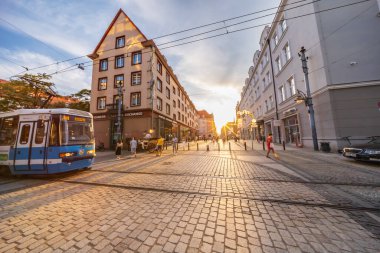 Wroclaw, Polonya - 31 Temmuz 2024: Wroclaw, Polonya 'daki Sunset' te Geleneksel Avrupa Mimarisi ile Tarihsel Arazi Taşı Sokağında Yürüyen Modern Mavi Elektrik Tramvayı