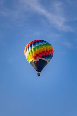 Altın saat boyunca kırmızı kiremitli binaların üstünde açık mavi gökyüzünde uçan renkli sıcak hava balonu.
