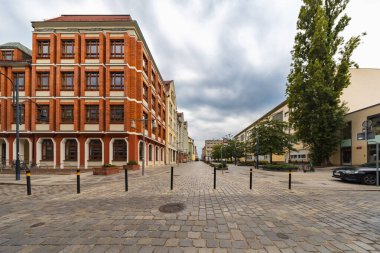 Wroclaw, Polonya - 2 Ağustos 2024: Wroclaw, Polonya 'da antika bir cadde, tarihi tuğla binalar ve bulutlu bir gökyüzü altında büyüleyici bir kaldırım taşı yolu, Avrupa mirası hissi uyandırıyor