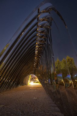 Wroclaw, Polonya - 24 Ağustos 2024: Wroclaw 'daki Daliowa Adası' nda gece aydınlatılmış Nawa heykeli, yıldızlı bir gökyüzü altında şehir ışıklarını yansıtan modern bir sanat kurulumu