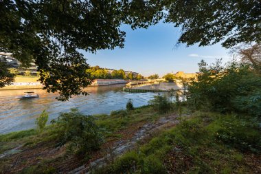 Wroclaw, Polonya - 30 Ağustos 2024: Bereketli ağaçlar ve nehir kenarındaki yeşillikler tarafından çerçevelenmiş güneşli Wroclaw şehri, aydınlık bir günde kentsel güzelliği yakalıyor