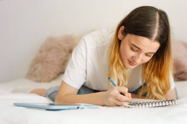 Genç bir kız yatak odasında resim yapıyor ya da ödev yapıyor. Evde okuyan bir genç. Okula geri dön.
