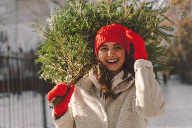 Kırmızı şapkalı güzel bir kız Noel ağacı taşıyor. Minimum moda festivali Noel ve Yeni Yıl kutlamaları konsepti.