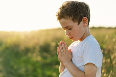 Boy closed her eyes and praying in a field at sunset. Hands folded in prayer concept for faith, spirituality and religion. clipart