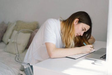 Genç bir kız yatak odasında resim yapıyor ya da ödev yapıyor. Evde okuyan bir genç. Okula geri dön.