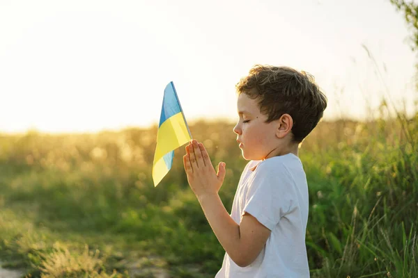 Ukrainian boy closed her eyes and praying to stop the war in Ukraine in a field at sunset. Hands folded in prayer concept for faith, spirituality and religion. War of Russia against Ukraine. Stop War