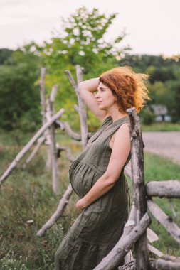 Güzel hamile bir kadın dışarıda, mutlu bir bebek bekliyor ve mutlu bir hamilelik dönemi geçiriyor. Hamilelik ve aile kavramları. Annelik. Hamile karnı. Bebek bekliyor.